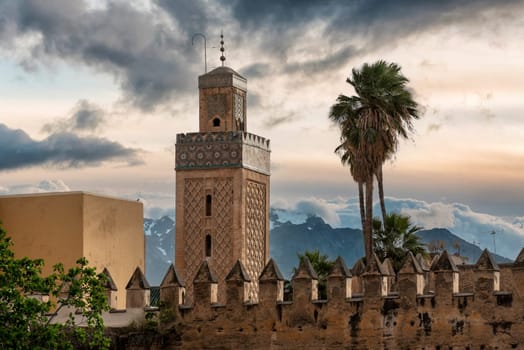 Minaret of an old mosque in Marrakech, Atlas mountains and a scenic sky in the background, Morocco