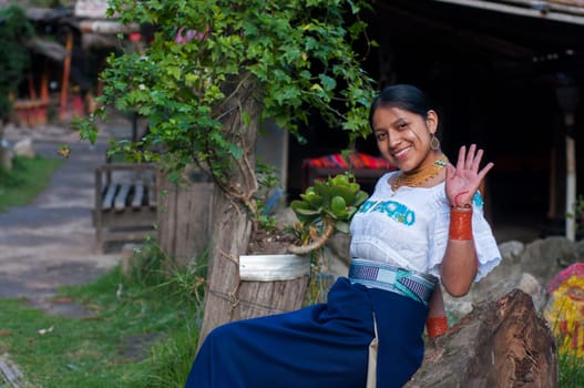 young indigenous woman waving to the camera, very happy and smiling sitting in her humble home in latin america. High quality photo