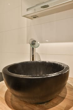 a black bowl sink on a wooden counter in a bathroom with white tile walls and wood flooring around it