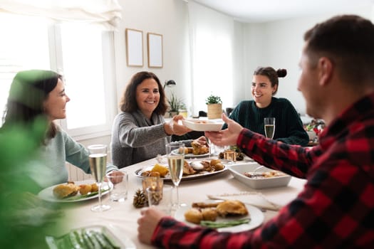 Mature caucasian woman pass plate of food to young man during family Christmas dinner. Holiday concept.