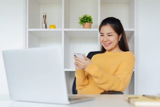 Young woman sitting in front of computer laptop and using mobile phone.