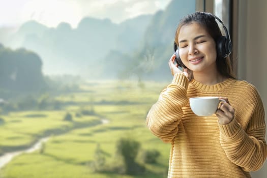 Young woman standing at the window she listening to music with headphones and looking at the view in the bedroom at resort.