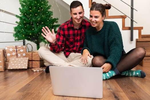 Young caucasian couple on video call celebrating Christmas with family. Waving hello. Using laptop. Holiday concept.