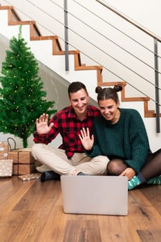 Young caucasian couple on video call celebrating Christmas with family. Waving hello. Using laptop. Vertical image. Holiday concept.