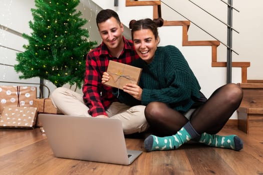 Young couple on a video call showing some Christmas presents to family. Social distancing Christmas. Holiday concept.