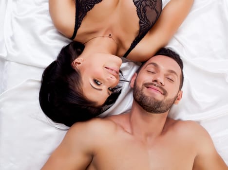Attractive sexual partners posing lying on satin sheets
