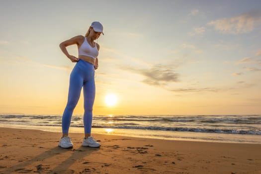 silhouette of a sports girl against the background of the sea at dawn, the girl stands in leggings and a top, in a cap against the background of the sea. High quality photo