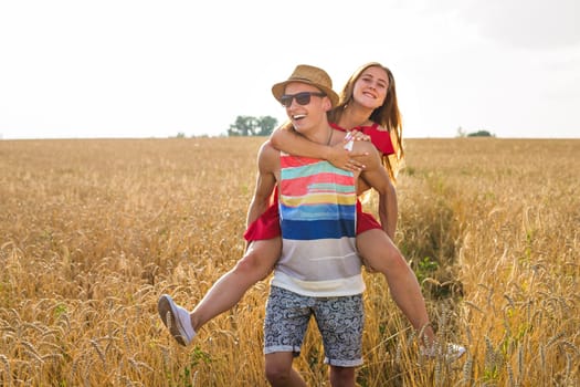 Happy Couple Having Fun Outdoors on wheat field over sunset. Laughing Joyful Family together. Freedom Concept. Piggyback.
