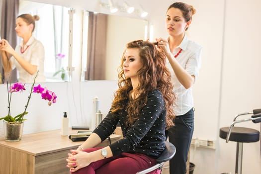 Professional hairdresser styling long woman curly hair.