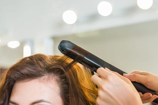 Curling hair in beauty salon. Professional hairdresser styling long woman curly hair.