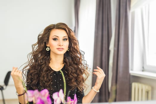 Portrait of elegant woman with curly hair looking at reflection in mirror.