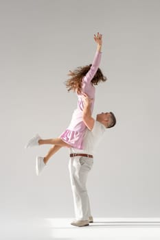 Beautiful young couple dancing on light background. Full length of young beautiful couple bonding while standing against white background