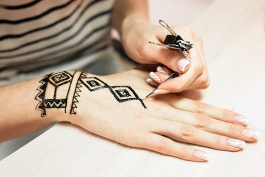 Process of applying Mehndi on female hand close up.