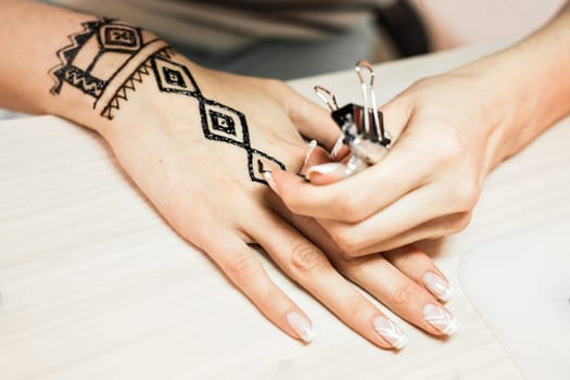 young woman mehendi artist painting henna on the hand.