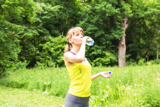 Fitness woman drinking water from bottle. Muscular young female taking a break from workout.