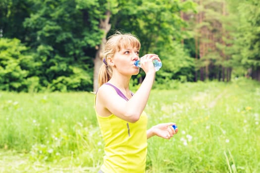 Fitness woman drinking water from bottle. Muscular young female taking a break from workout.