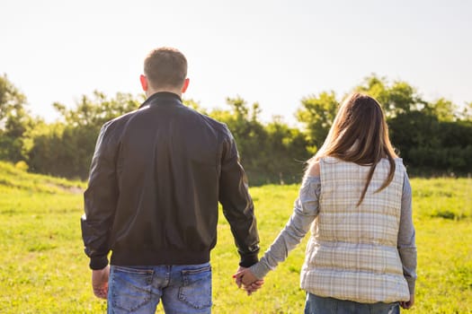 rear view of couple holding hands walking in autumn countryside.