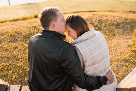 Romantic young couple enjoying a date sitting in a close embrace on a park bench overlooking a lake, view from behind