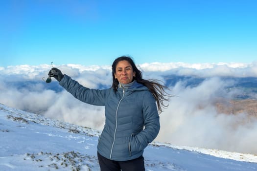 portrait of latin woman smiling in the snow, with warm clothes above the clouds, on the top of the mountain of sierra nevada