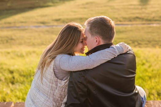 Romantic young couple enjoying a date sitting in a close embrace on a park bench overlooking a lake, view from behind