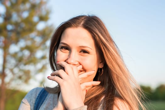 Surprised young woman with hands over her mouth outdoor.