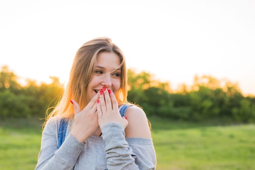 Surprised young woman with hands over her mouth outdoor.