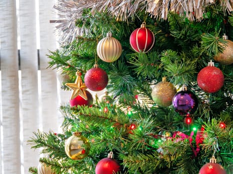 Red, golden, purple balls and color electtric lights decorating artificial Christmas tree.Close up look