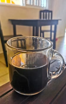 Glass cup of black coffee from Mexico on wooden background in clean kitchen.