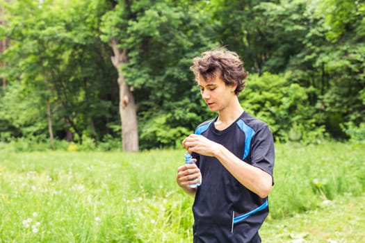 Athletic sport man drinking water from a bottle. Cold drink after outdoor fitness.