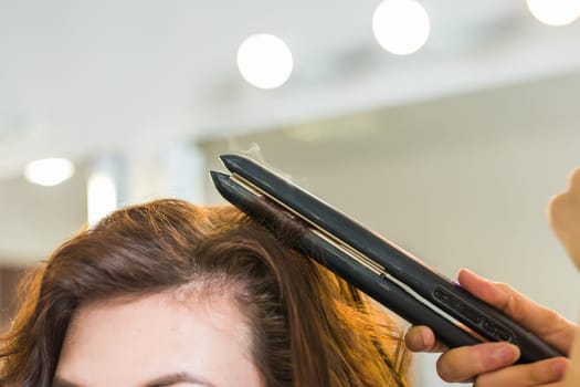 Close up of stylist's hand using curling iron for hair curls