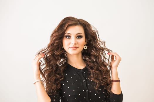beauty, hairstyle and people concept - happy young woman with hairdresser finishing hairdo at salon.