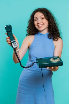 Hey you, call me back. Young woman talking on wired landline vintage telephone of 80s, advertising proposition of conversation, online shopping. Adult girl isolated on blue studio background. Vertical