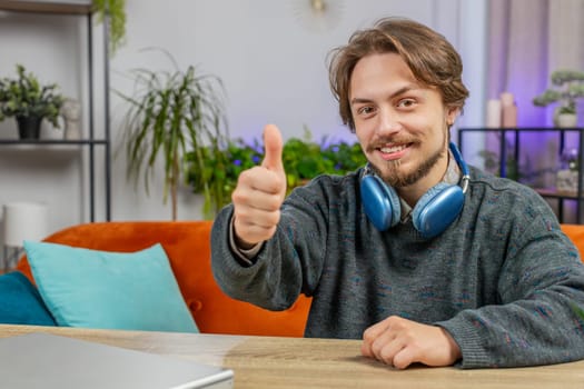 Like. Happy excited Caucasian man looking approvingly at camera showing thumbs up like sign positive something good great news positive feedback. Young smiling guy sitting at home office room at table