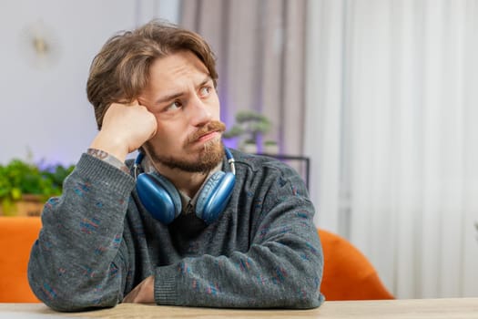 Portrait of sad Caucasian man guy sitting at home table looks pensive thinks over life concerns or unrequited love suffers from unfair situation. Problem break up depressed feeling bad annoyed burnout