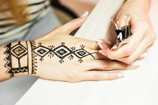 Artist applying henna tattoo on women hands. Mehndi is traditional Indian decorative art. Close-up.