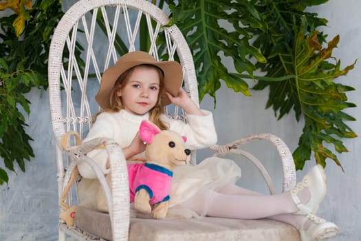 Little girl in big hat sits in a white chair