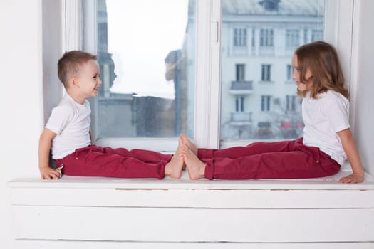 boy and girl sitting on the window sill by the window