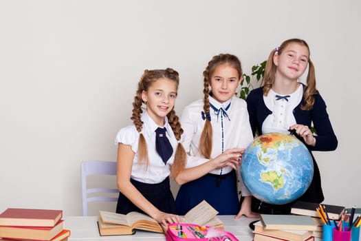 three schoolgirl girls at the desk watch the globe in a geography class