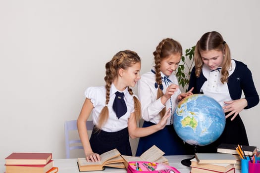 three schoolgirl girls at the desk watch the globe in a geography class