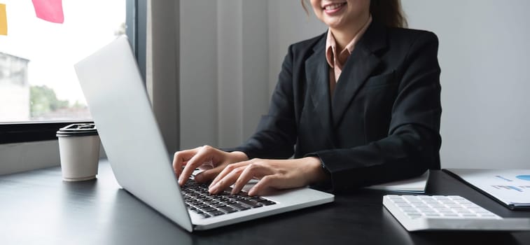 Professional Asian business woman intent on work focusing on laptop in modern office.