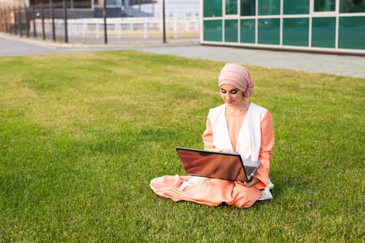 Young Muslim Girl using laptop and sitting on the grass