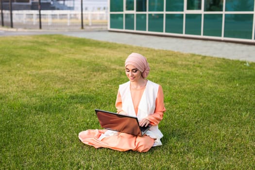 Young Muslim Girl using laptop and sitting on the grass