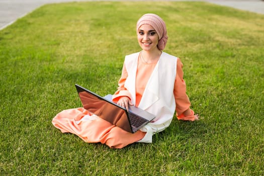 Young Muslim Girl using laptop and sitting on the grass