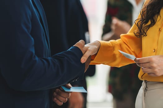 Businessmen shaking hand and making a contract in the sign of agreement, cooperation with businesswoman. Cropped image of managers holding business cards. Their partners standing behind. Intellectual.