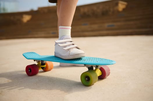 Closeup multicolored skate wheels and foot or leg on back of child or kid girl playing skateboard, or surf skate and start on outdoor pump track in skatepark by extreme sports. Kids entertainment