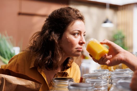 Storekeeper showing products to woman shopping in zero waste grocery store, inviting her to smell them. Merchant in local neighborhood shop suggesting food item to customer