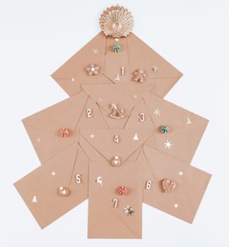 Creative Christmas tree advent calendar from craft envelopes, wooden numbers, cookies and christmas decor on a white background, top view close-up. Vertical photo.