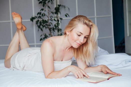 Woman reads a book in the bedroom on the bed