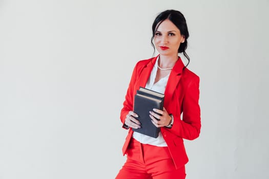 A young woman in a business suit, with a red book in hand, sitting on the wooden floor with a thoughtful face, glance to the side, full height.