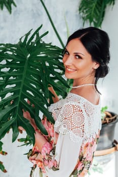 Beautiful brunette young woman relaxing and posing for camera on pink wall backgrorund. Lifestyle portrait of happy cheerful smiling adult caucasian female stands near palm tree with green branches